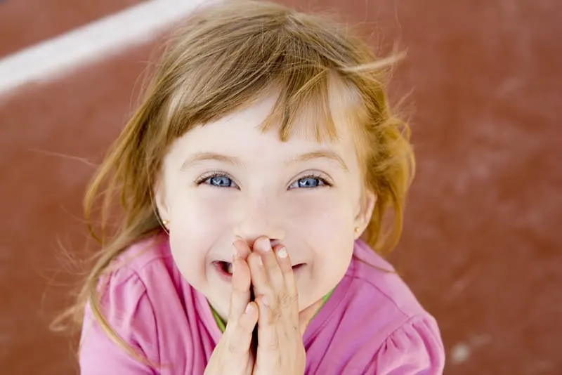 niedlichen kleinen Mädchen hält die Hände auf den Mund und lächelnd im Freien stehen