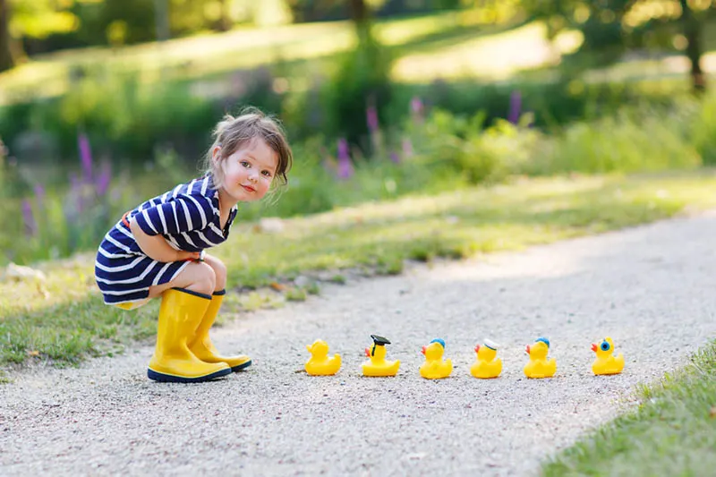 niedlichen kleinen Mädchen in gelben Stiefeln spielen mit Gummi-Enten im Freien