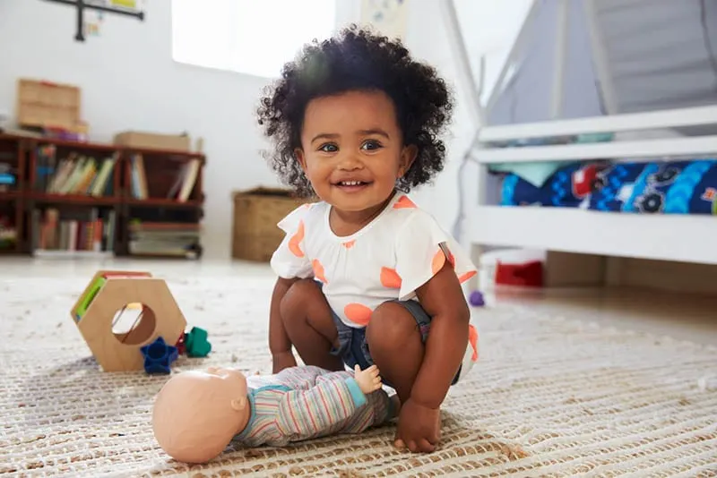 niedlichen kleinen Mädchen mit lockigem Haar spielen mit Spielzeug auf dem Boden