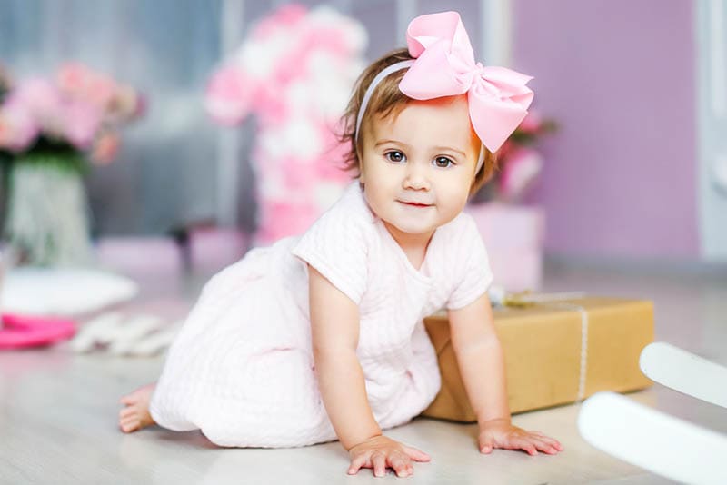 niedlichen kleinen Mädchen mit rosa Schleife auf dem Kopf auf dem Boden krabbeln
