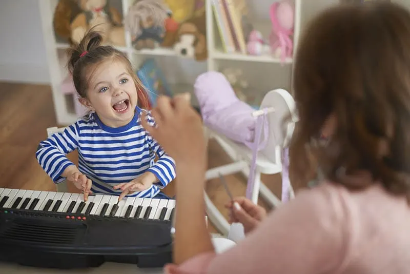 niedlichen kleinen Mädchen sitzen und singen mit ihrer Mutter neben dem Musikinstrument