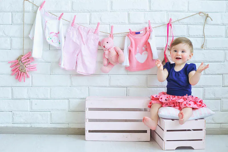 niedlichen kleinen lächelnden Mädchen mit Baby-Kleidung hängen hinter an der Wand