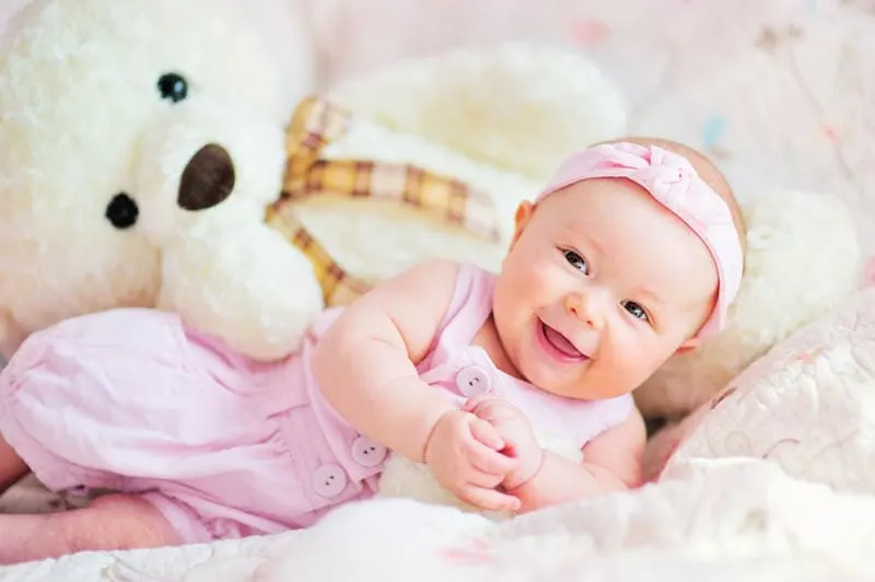 niedlichen lächelnden Baby Mädchen mit Teddybär Spielzeug auf dem Bett