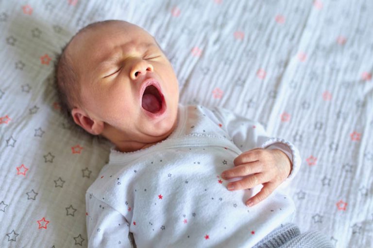 neugeborenes Baby liegt auf dem Bett und gähnt