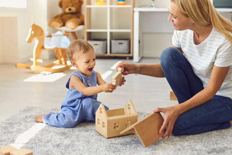 schöne Mutter gibt ein Spielzeug zu niedlichen Baby-Mädchen auf dem Boden