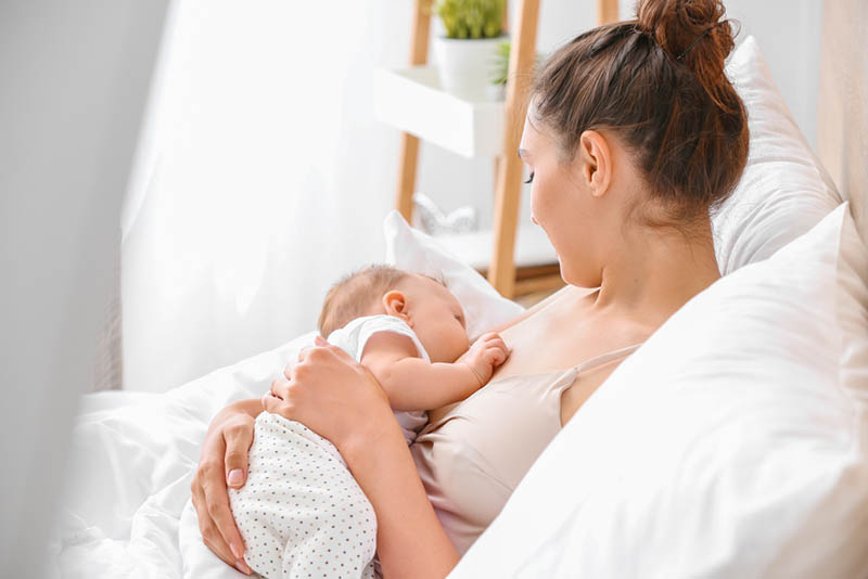 schöne Mutter stillt ihr Baby auf dem Bett