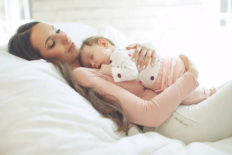 schöne junge Mutter hält schlafendes Baby auf der Brust