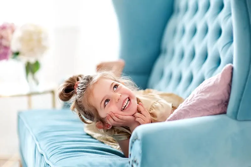 schöne kleine Mädchen spielen auf der blauen Couch zu Hause