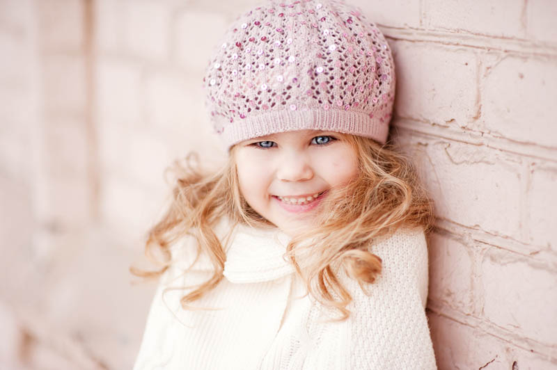 schönes Mädchen mit blonden Augen trägt einen Hut an der Wand stehen im Freien