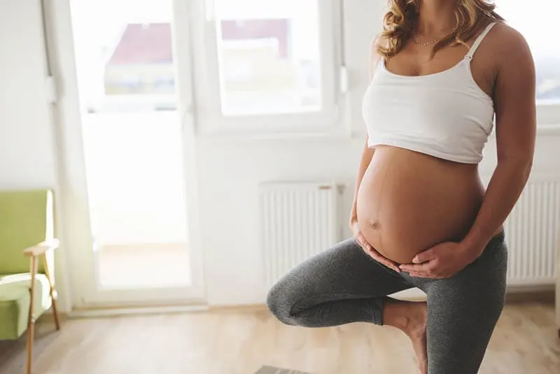 schwangere Frau, die auf einem Bein steht, während sie zu Hause trainiert