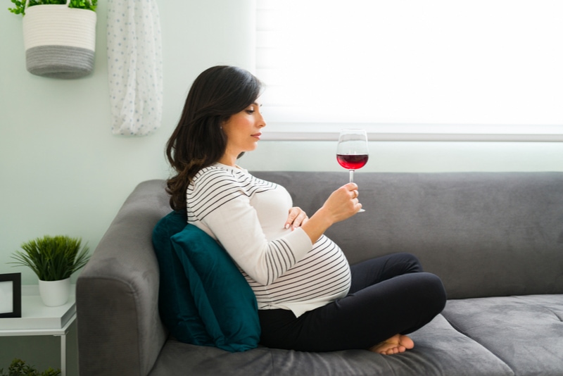 schwangere Frau, die entscheidet, ob sie ein Glas Wein trinkt oder nicht