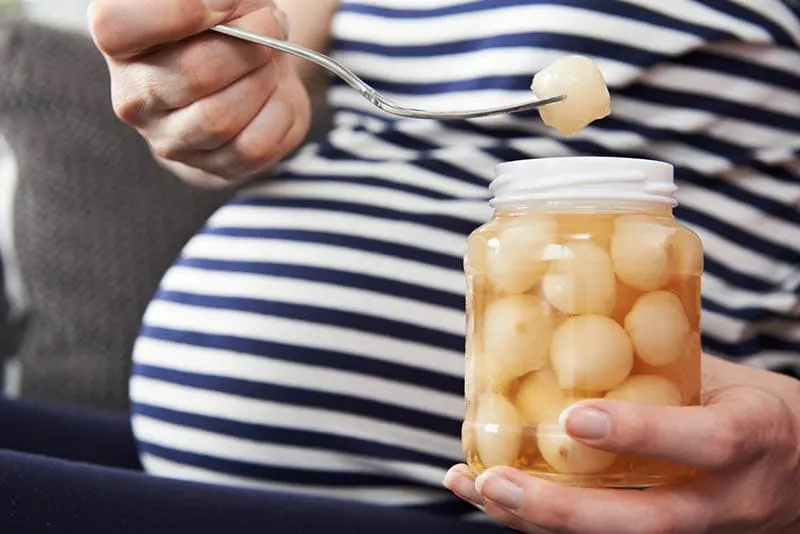 schwangere Frau hält ein Glas und Kiefer von eingelegten Zwiebeln