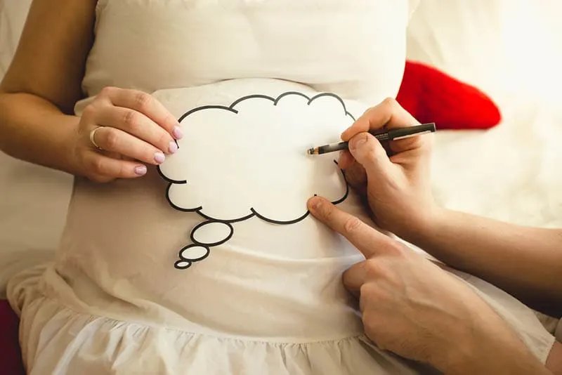 schwangere Frau hält einen Aufkleber, während Mann darauf schreibt