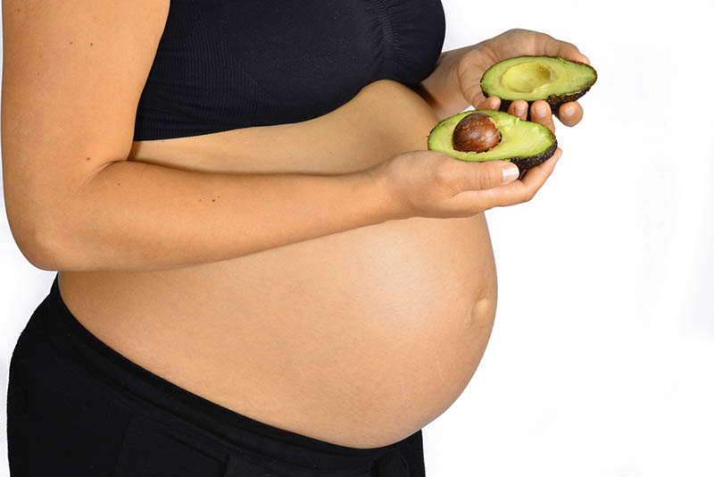 schwangere Frau in Sportkleidung hält eine Avocado