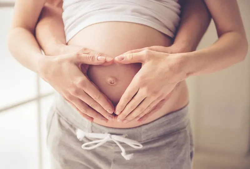 schwangere Frau mit Ehemann macht Herzform mit Händen auf dem Bauch
