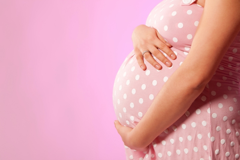 schwangere Frau mit den Händen über Bauch am rosa Hintergrund