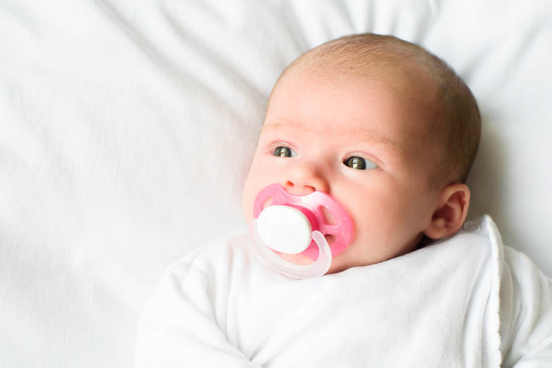 süße neugeborenes Baby auf dem Bett liegend und saugen rosa Schnuller