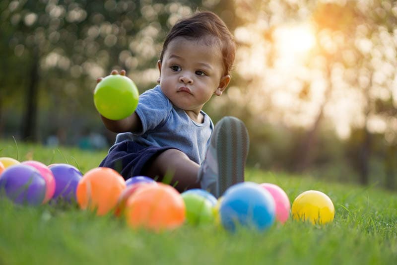 süßes Baby Junge sitzt auf dem Gras im Freien mit bunten spielen Bälle