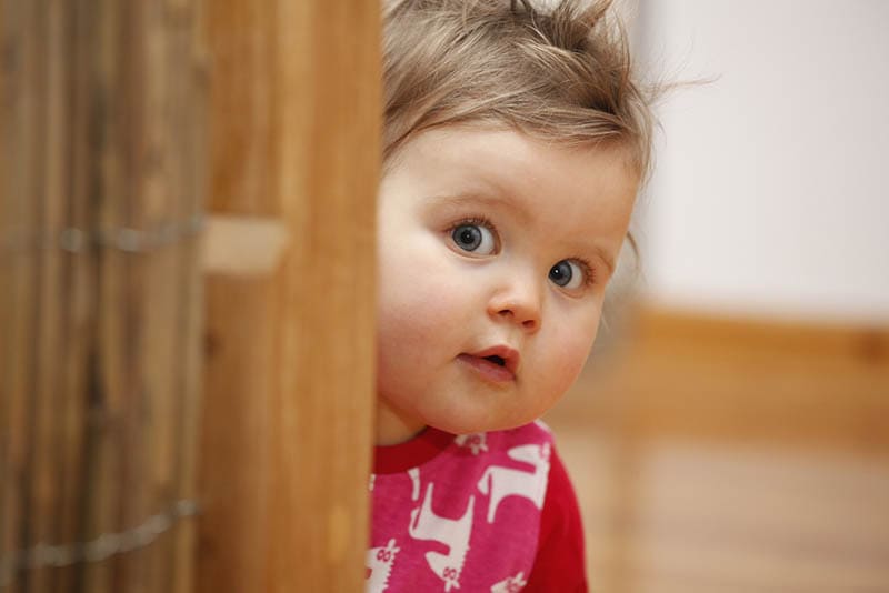 süßes Baby Mädchen mit dicken Wangen zu Hause versteckt