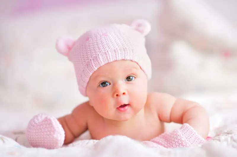 süßes Baby Mädchen mit rosa Hut auf dem Bauch liegend