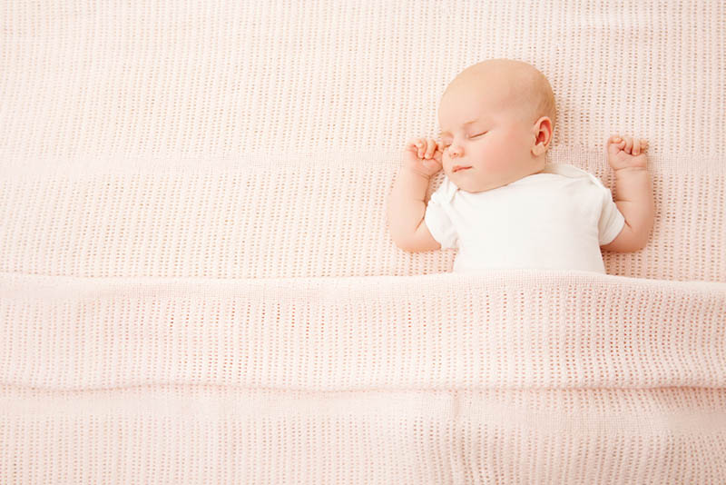 süßes Baby Mädchen schlafen im Bett mit rosa Decke bedeckt