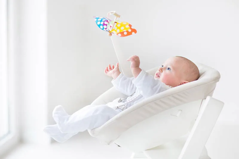 süßes Baby in der Babywippe liegend und mit Blick auf bunte Schmetterling Spielzeug