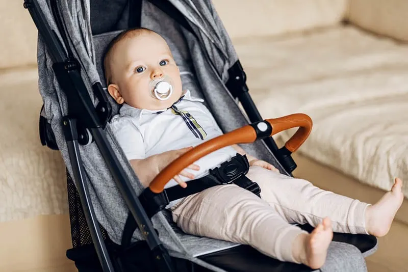 süßes Baby mit Schnuller sitzen in einem Kinderwagen im Haus