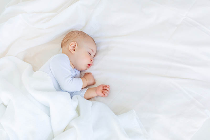 süßes Baby schlafend auf dem Bett mit weißem Laken bedeckt