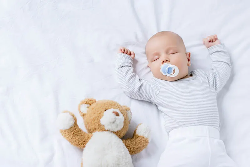 süßes Baby schläft mit Schnuller im Bett und mit Teddybär Spielzeug