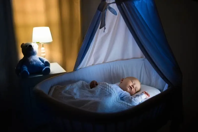 süßes Baby schläft nachts im Stubenwagen im Schlafzimmer