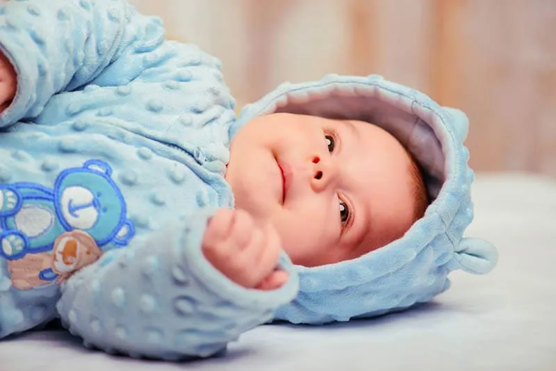 süßes Baby trägt einen blauen Körper Anzug und liegt auf dem Bett