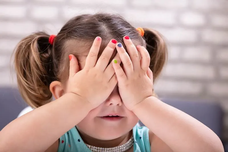 süßes kleines Mädchen bedeckt ihre Augen mit den Händen und zeigt ihren Nagellack