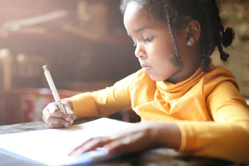 süßes kleines Mädchen sitzt am Tisch und schreibt auf Papier