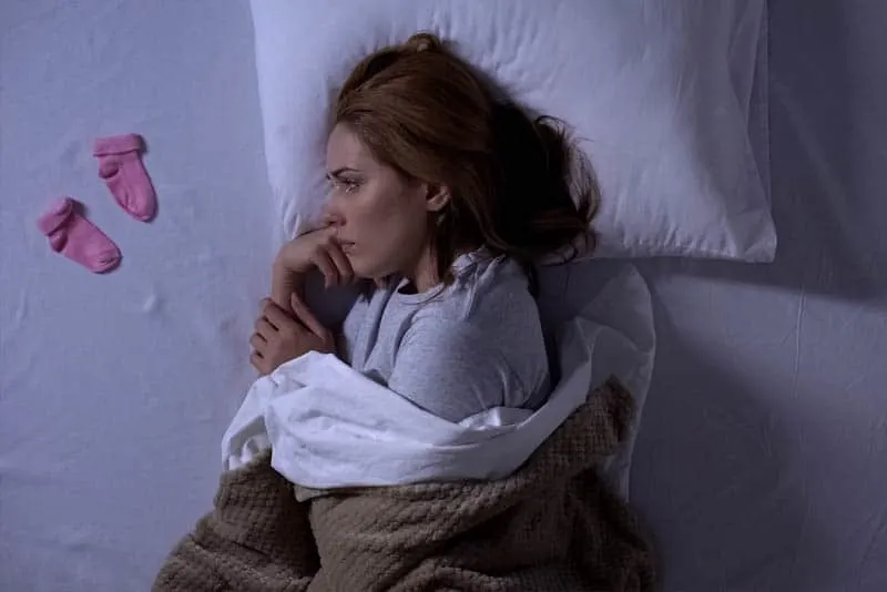 traurige junge Frau im Bett liegend und weinend beacuse der Fehlgeburt und Blick auf Baby-Socken
