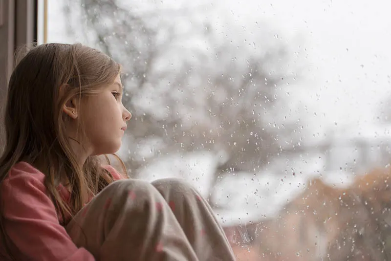 trauriges kleines Mädchen schaut durch das regnerische Fenster