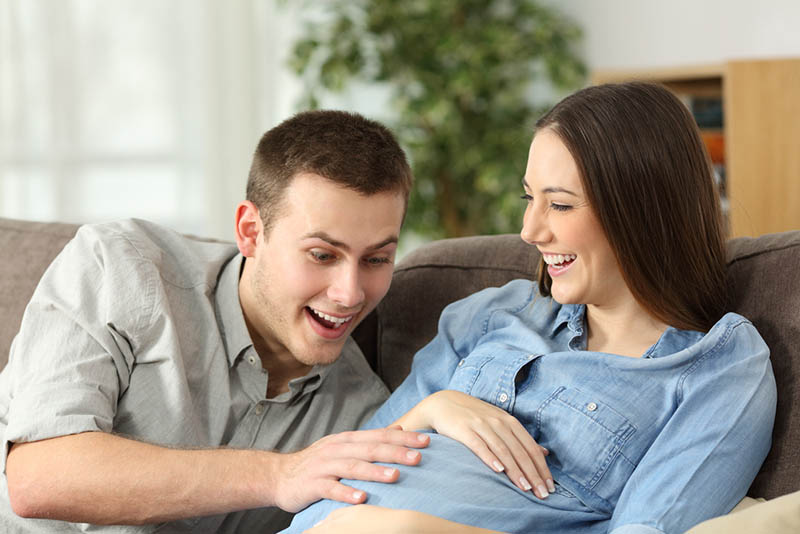 überrascht Mann streichelt schwangere Frau Bauch auf der Couch