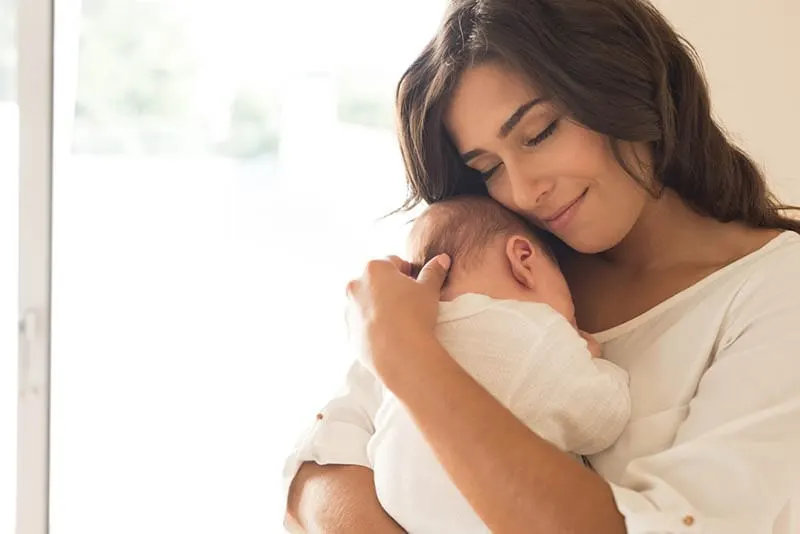 ziemlich lächelnd Mutter hält und kuscheln mit ihrem Baby auf der Brust