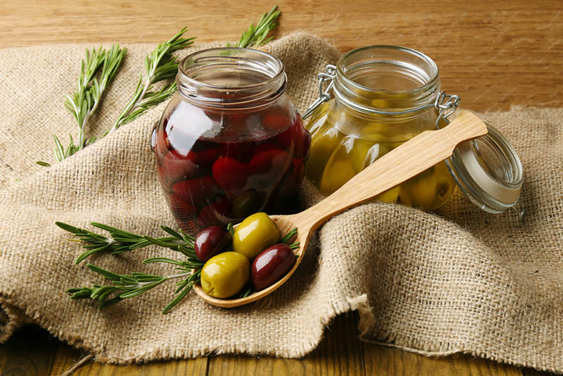 zwei Gläser mit Oliven und ein Löffel mit Oliven auf dem Holztisch