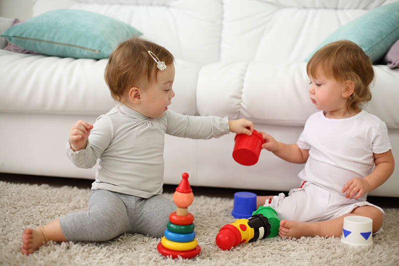 zwei barfuß Kinder sitzen auf Teppich und spielen mit bunten Spielzeug in der Nähe von Sofa