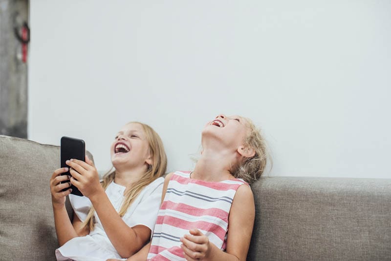 zwei blonde Schwestern auf der Couch lachend am Handy
