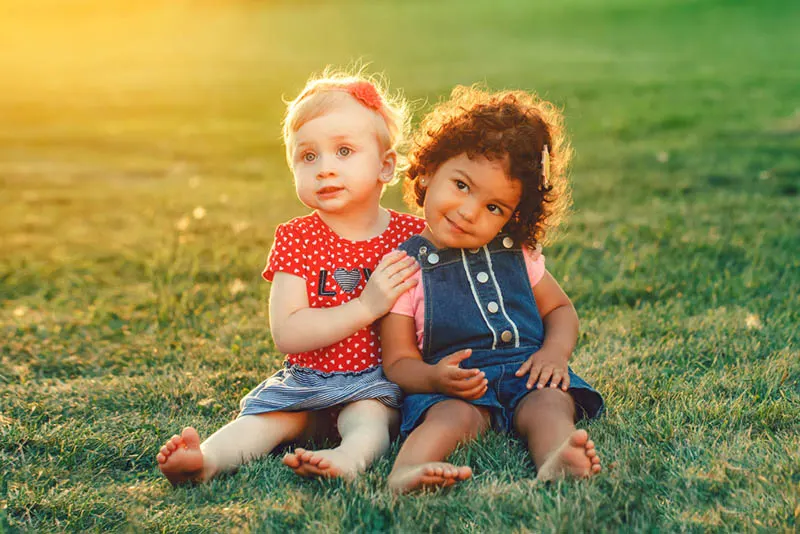 zwei niedliche Baby-Mädchen sitzen auf dem Gras und posieren in der Umarmung