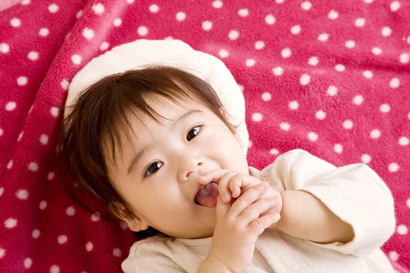Baby Mädchen setzen Hand in den Mund, während auf dem Bett liegend