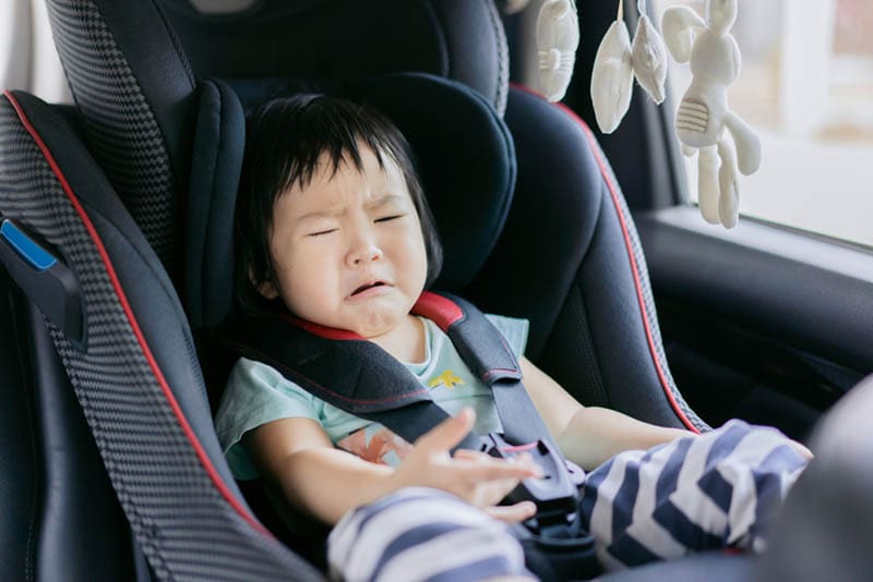 Baby Mädchen weint in einem Autositz mit Sicherheitsgurten auf