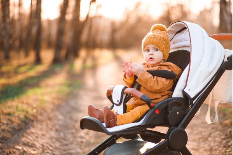 Baby in warmer Jacke und Hut, die im modernen Kinderwagen auf einem Spaziergang in einem Park sitzen