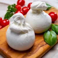 zwei Kugeln Burrata-Käse mit Tomaten auf dem Schneidebrett