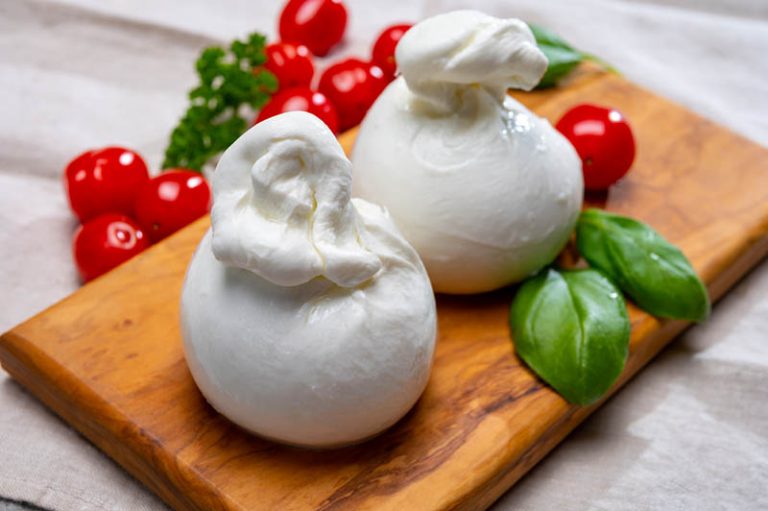 zwei Kugeln Burrata-Käse mit Tomaten auf dem Schneidebrett