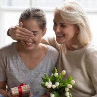 Ältere Frau überrascht ihre Schwiegertochter mit Geschenk und Blumen