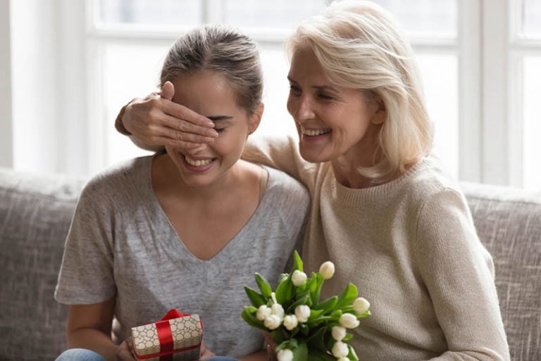 Ältere Frau überrascht ihre Schwiegertochter mit Geschenk und Blumen
