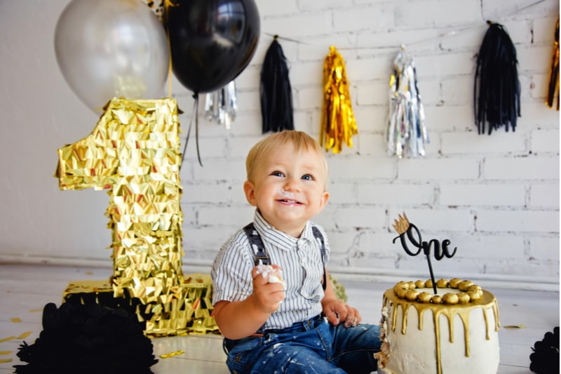 Glücklicher Junge Blondine 1 Jahr alt an seinem Geburtstag versucht Süßigkeiten