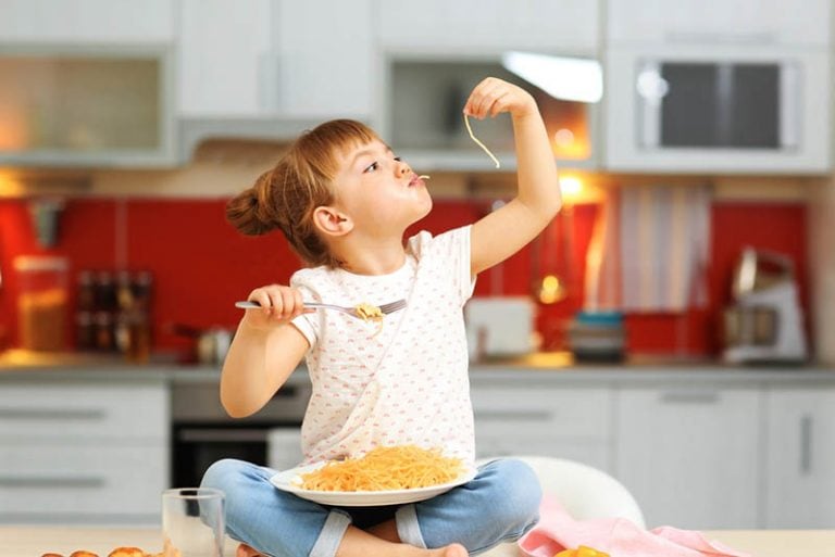 niedlichen kleinen Mädchen sitzen auf dem Tisch und essen Spaghetti